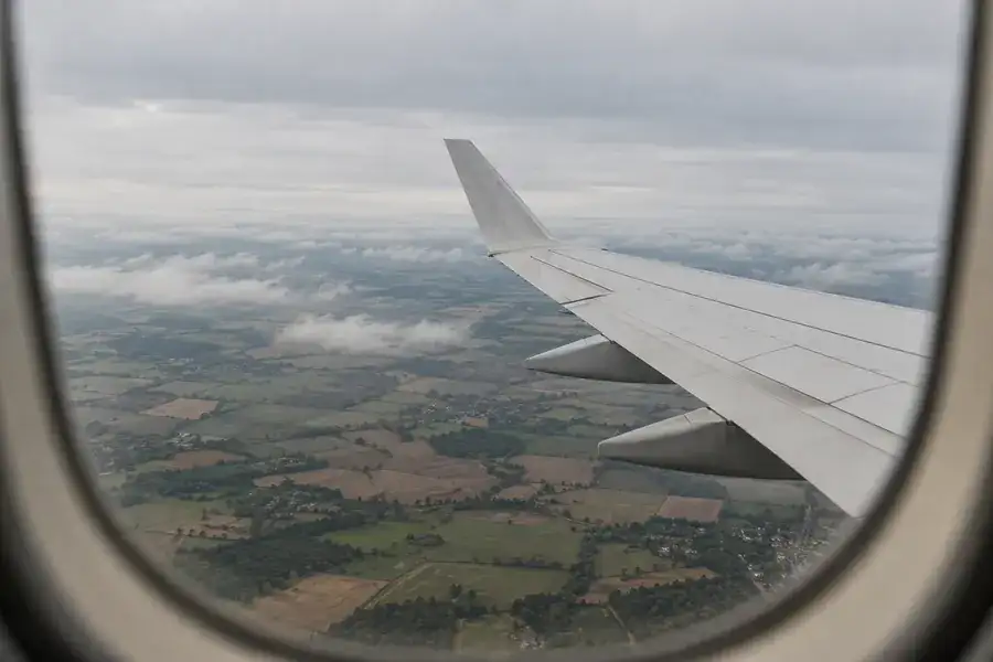 View from an aircraft window of the wing above farmland and low cloud